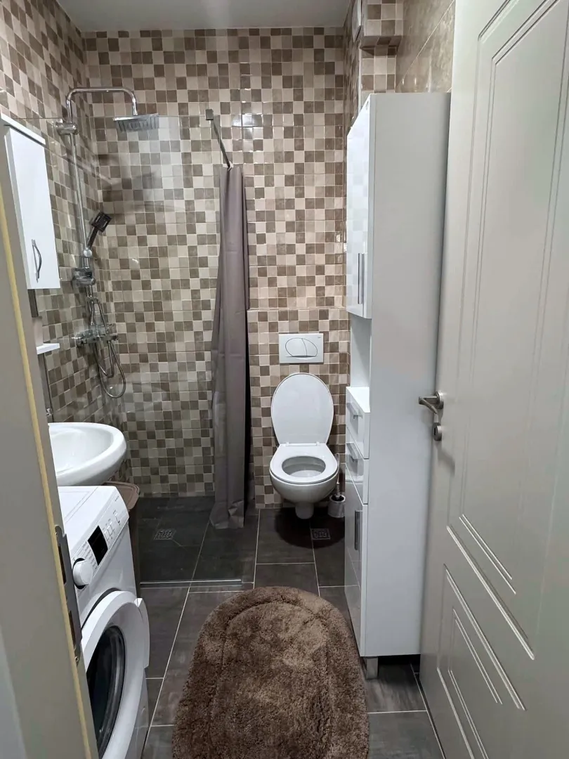 Compact bathroom with a shower cabin, washbasin, toilet, and washing machine.