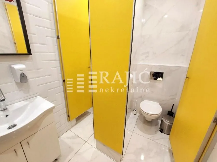 View of a modernly equipped restroom with yellow partition stalls.
