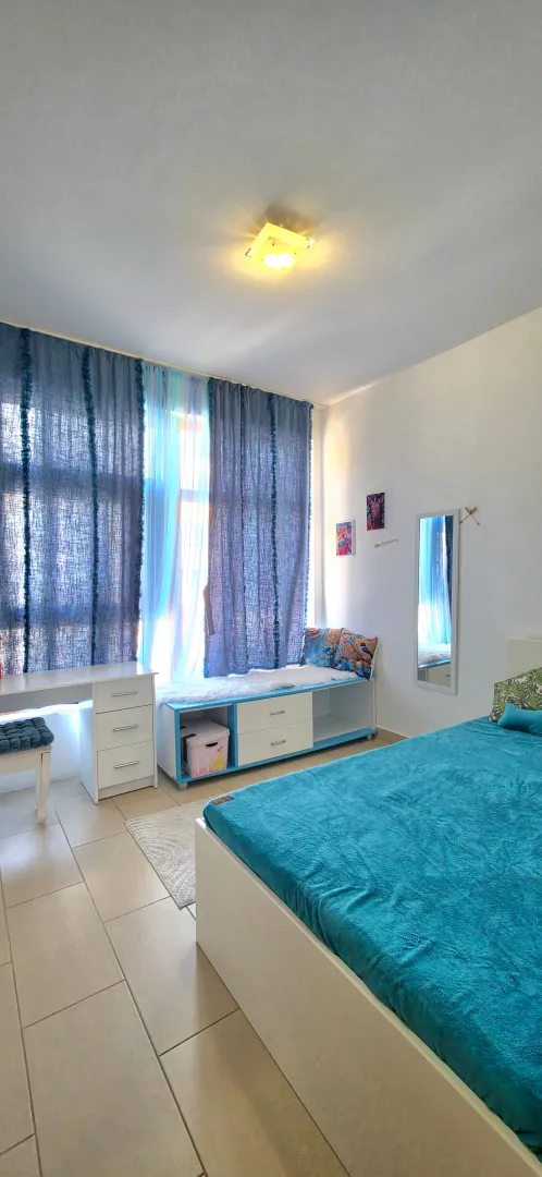 Bright and tidy bedroom with a bed, desk, and blue curtains.