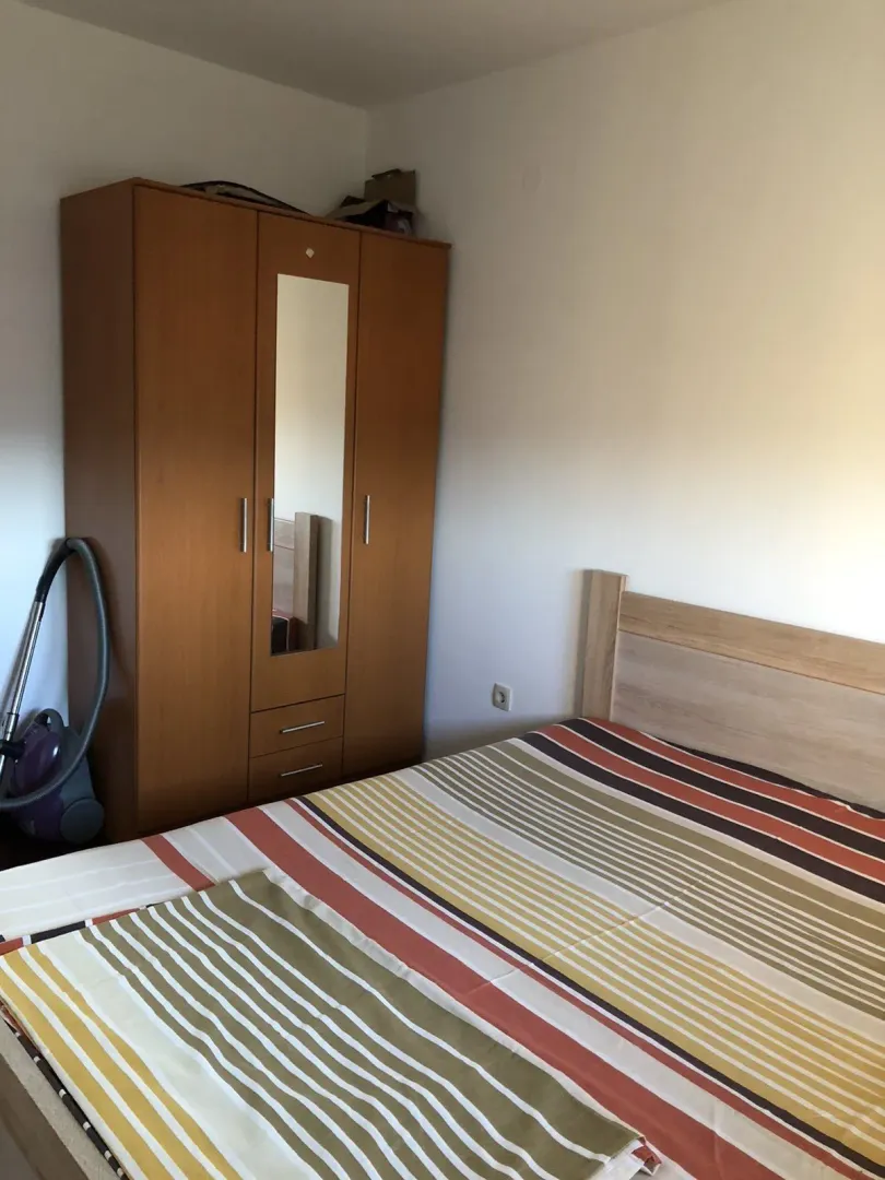 Simple furnished bedroom with a wooden wardrobe and a bed.