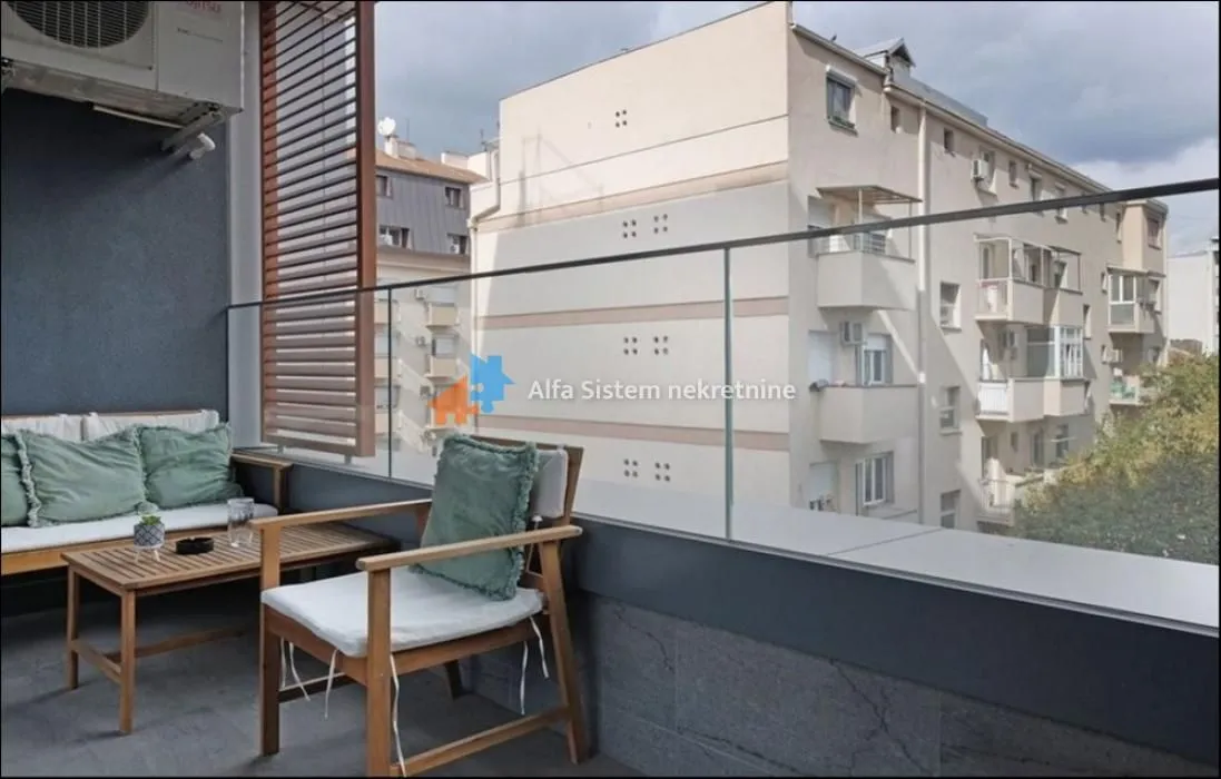 Namešten balkon sa garniturom za sedenje i pogledom na okolne zgrade.