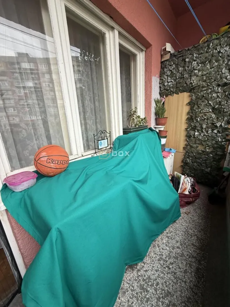 Manji zatvoreni balkon sa pokrivenim nameštajem i košarkaškom loptom.