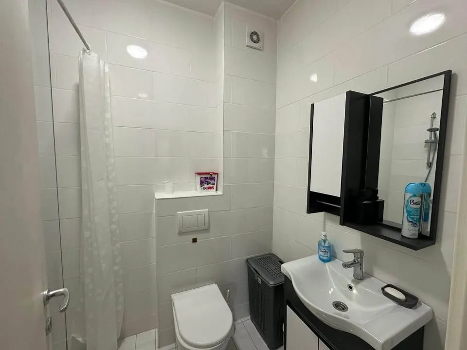 Kupatilo opremljeno umivaonikom, WC šoljom i tuš kabinom sa zavjesom.