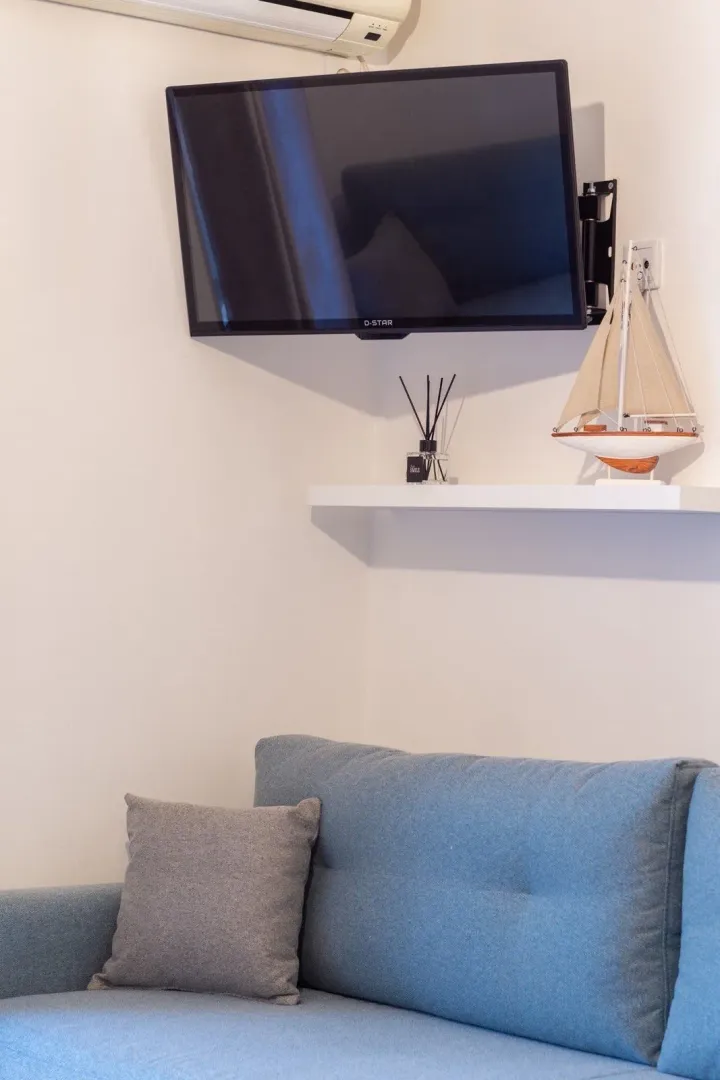 Part of the living room with a sofa, wall-mounted TV, and a shelf with decorations.