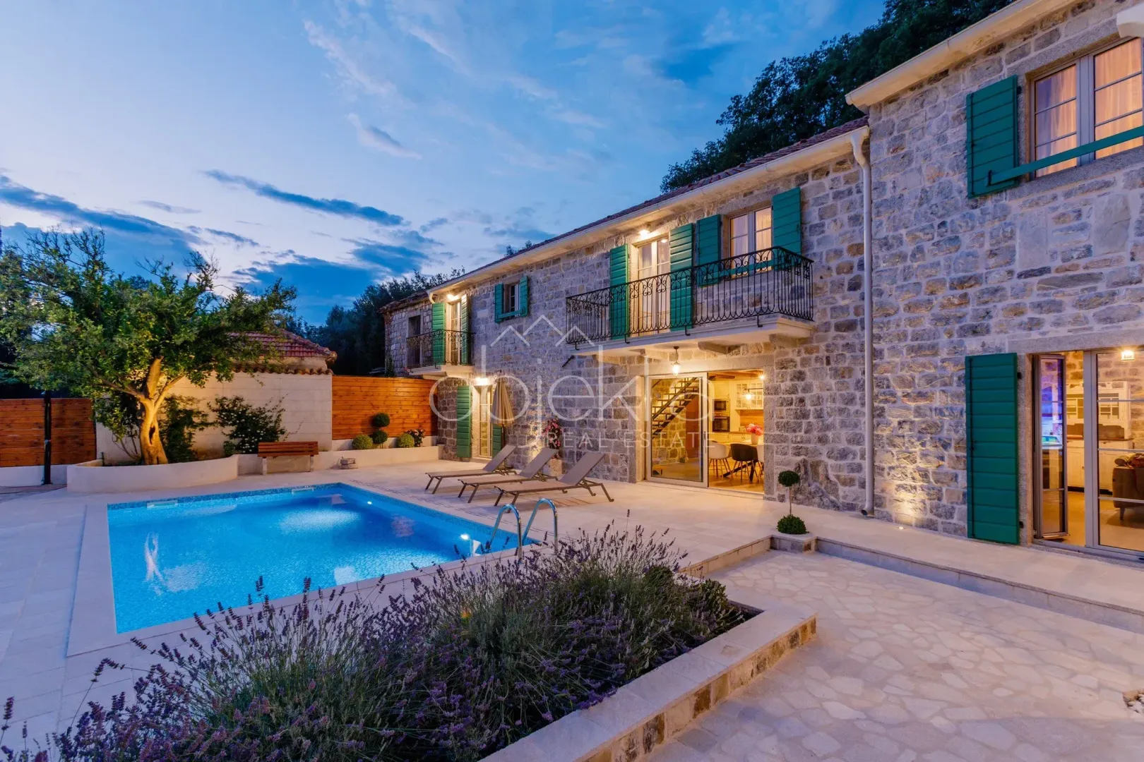 View of a stone house with a swimming pool and landscaped yard at dusk.