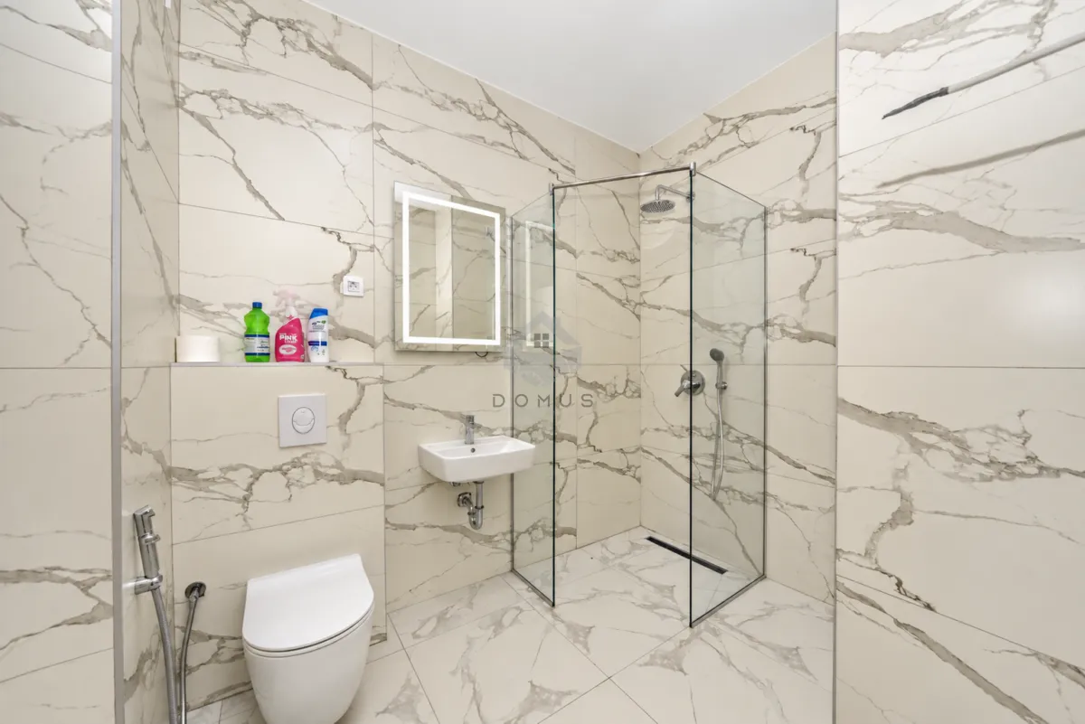 Modern bathroom tiled with marble-look tiles, featuring a walk-in shower and a wall-mounted toilet.