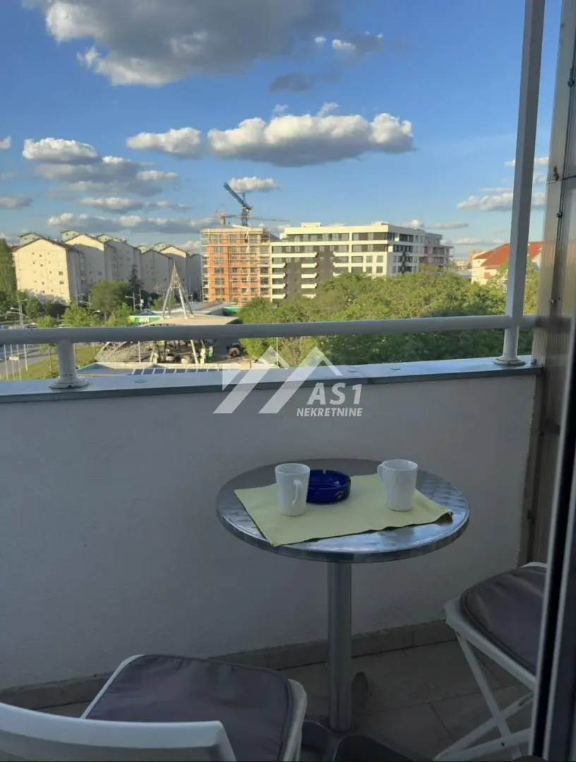Manji balkon sa stolom i dve stolice i pogledom na grad.