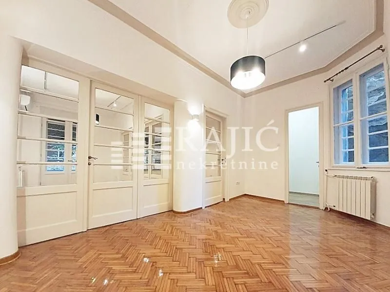 Empty room with wooden parquet flooring and white double doors.