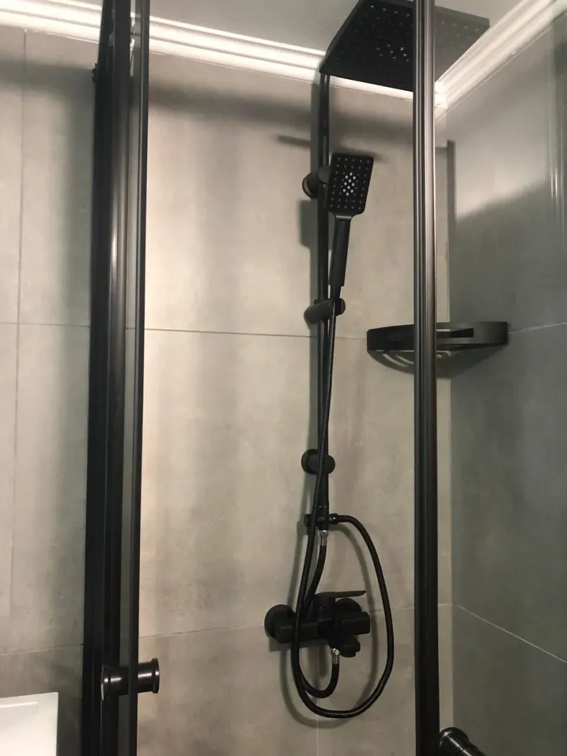 Shower cabin with black fixtures and gray tiles.