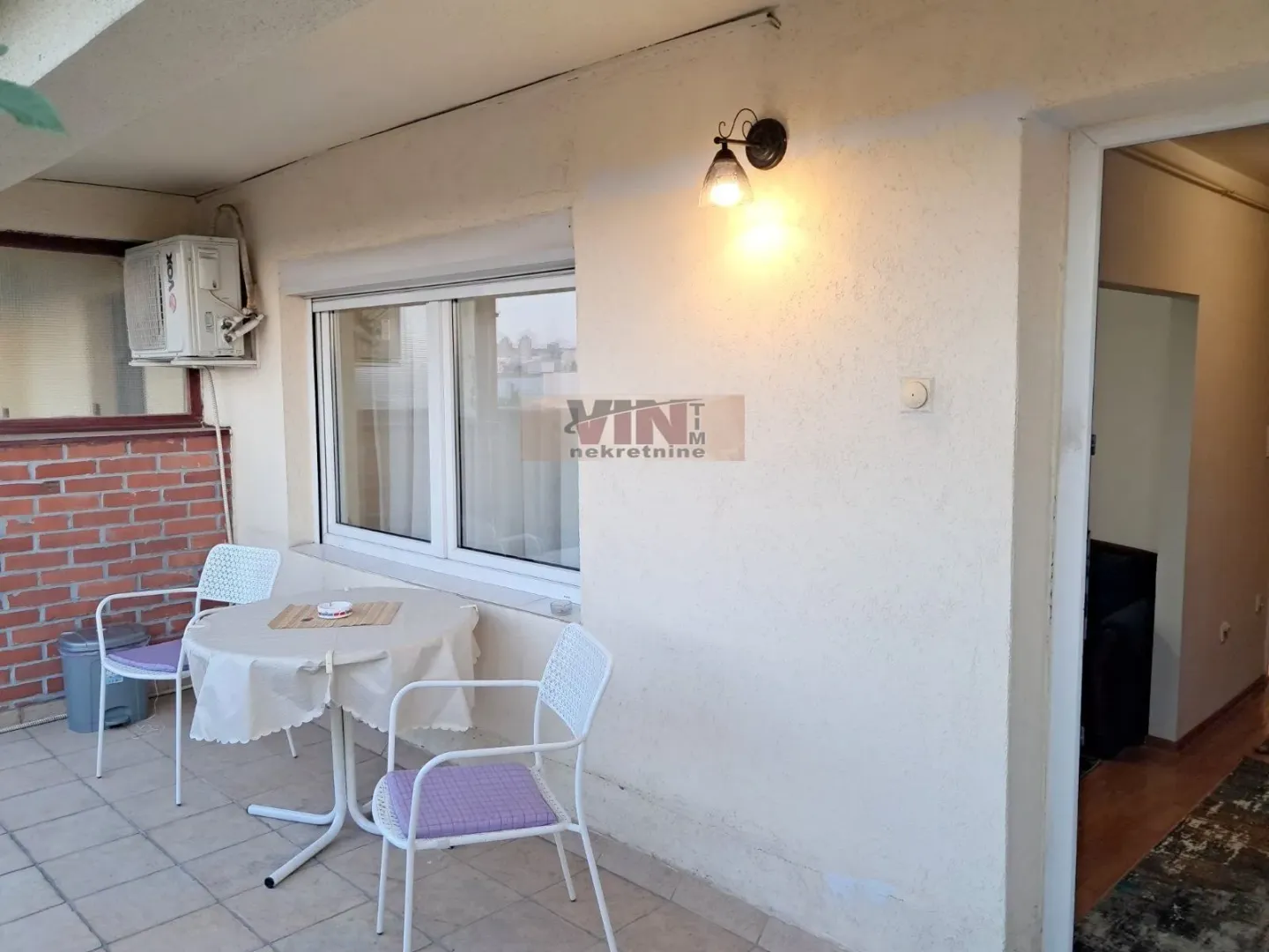 Covered terrace with a table, chairs, and an air conditioning unit.
