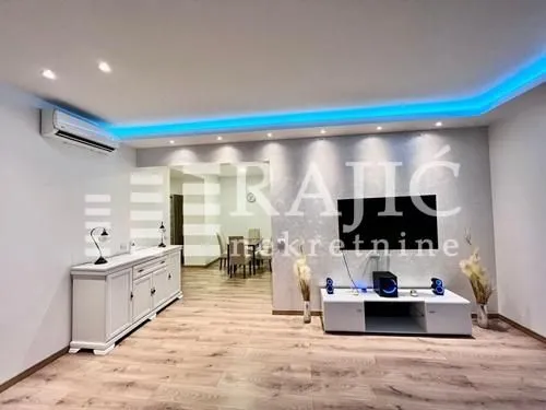 Living room with TV console and dining area in the background.