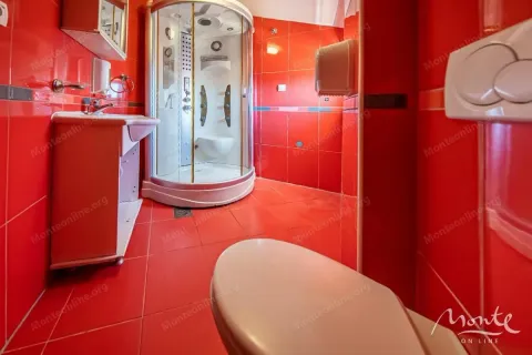 Kupatilo obloženo crvenim pločicama sa tuš kabinom, umivaonikom i toaletom. - image 6