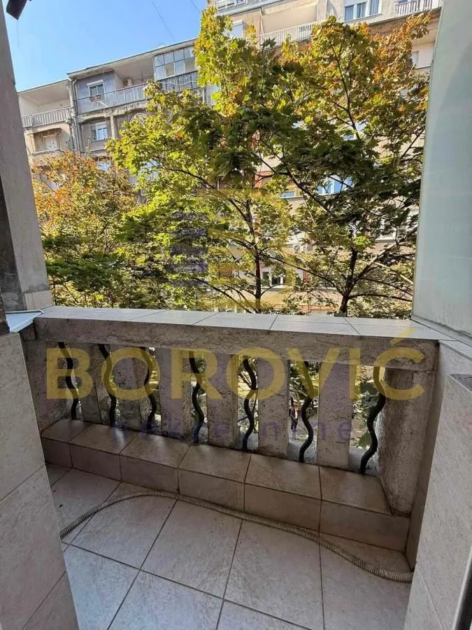 Manji popločani balkon sa pogledom na drveće i susedne zgrade.