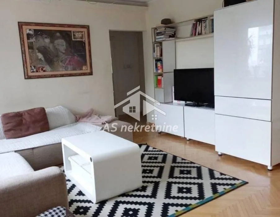 Living room with a sofa, TV, and white furniture units.