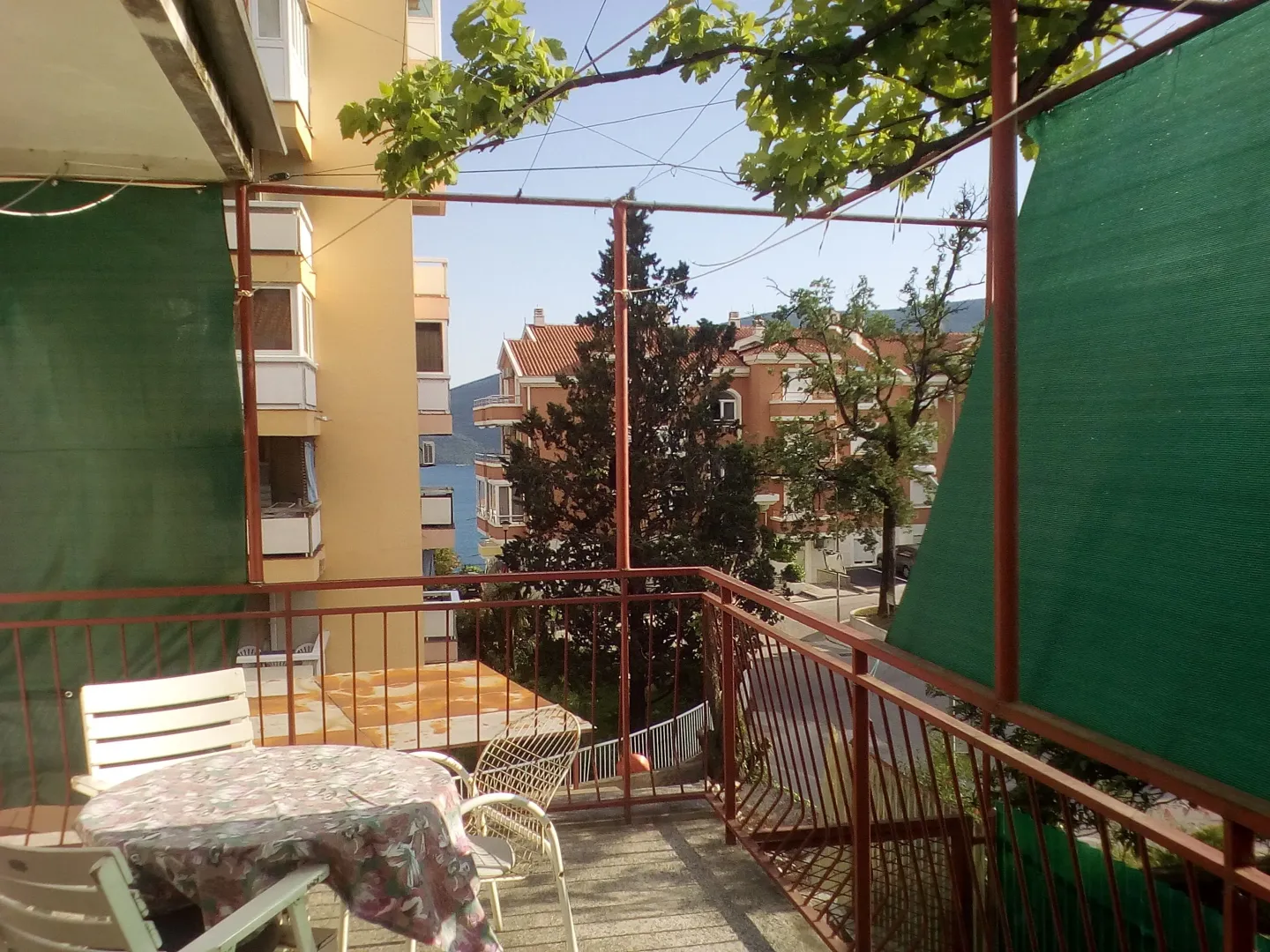 Furnished terrace with a table, chairs, and a view of surrounding buildings and greenery.