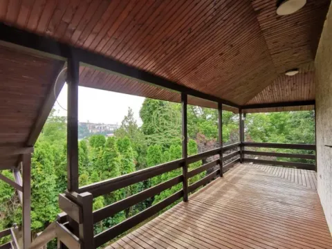 Covered wooden terrace with a railing and a view of greenery. - image 13