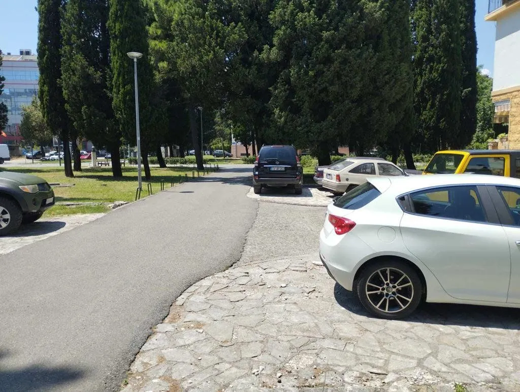 Parking area in front of the building with green space and cypress trees.