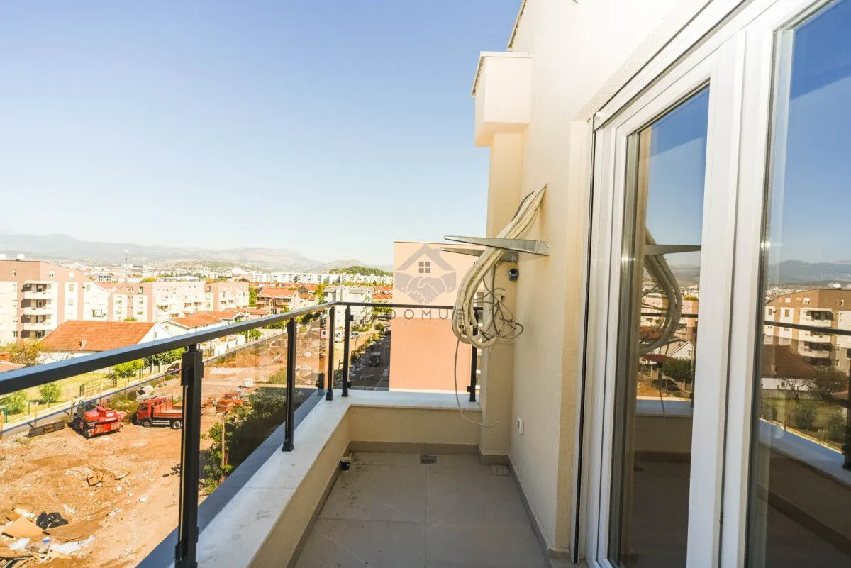 Manji popločani balkon sa staklenom ogradom i pogledom na grad.