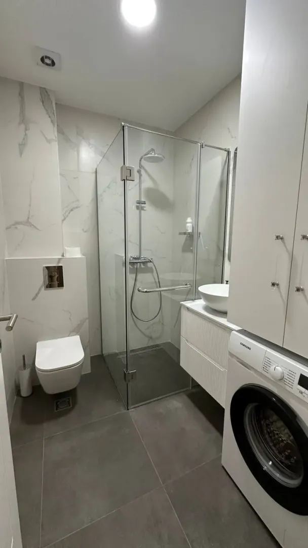 Moderne kupatilo sa tuš kabinom, WC šoljom i veš mašinom.