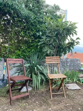 Dvije drvene stolice u dvorištu okružene zelenilom i kamenim zidom. - image 3