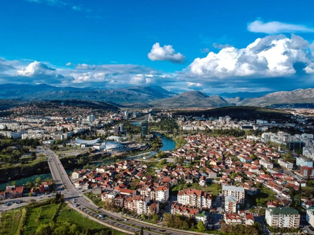 Pogled iz vazduha na grad sa rijekom i planinama u pozadini.