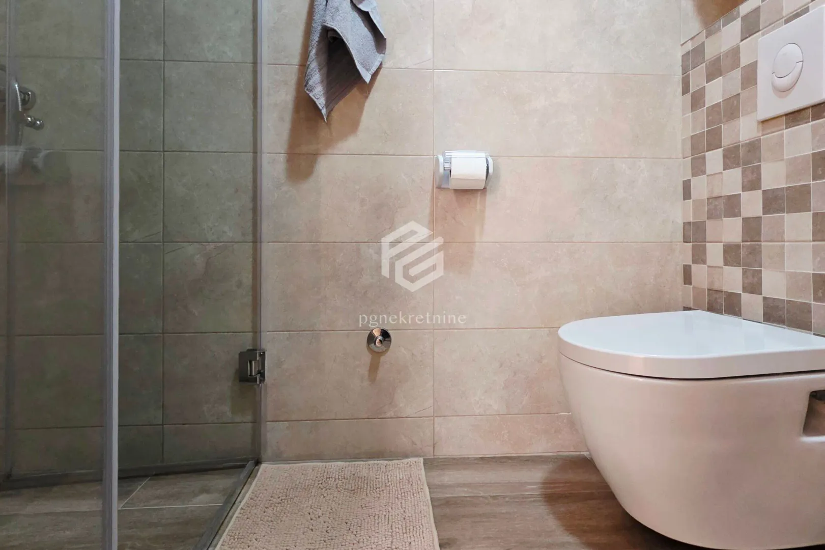 View of the bathroom with a walk-in shower and a wall-mounted toilet.