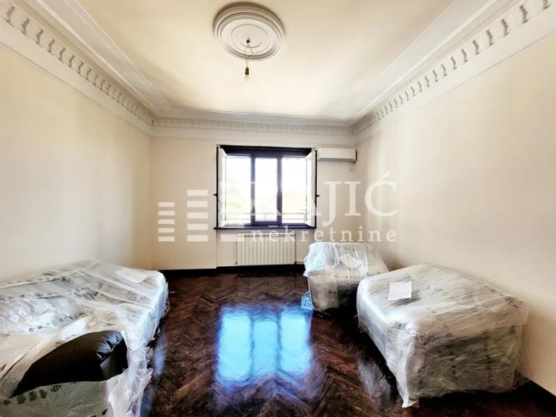 Empty room with parquet flooring and furniture covered in plastic wrap.