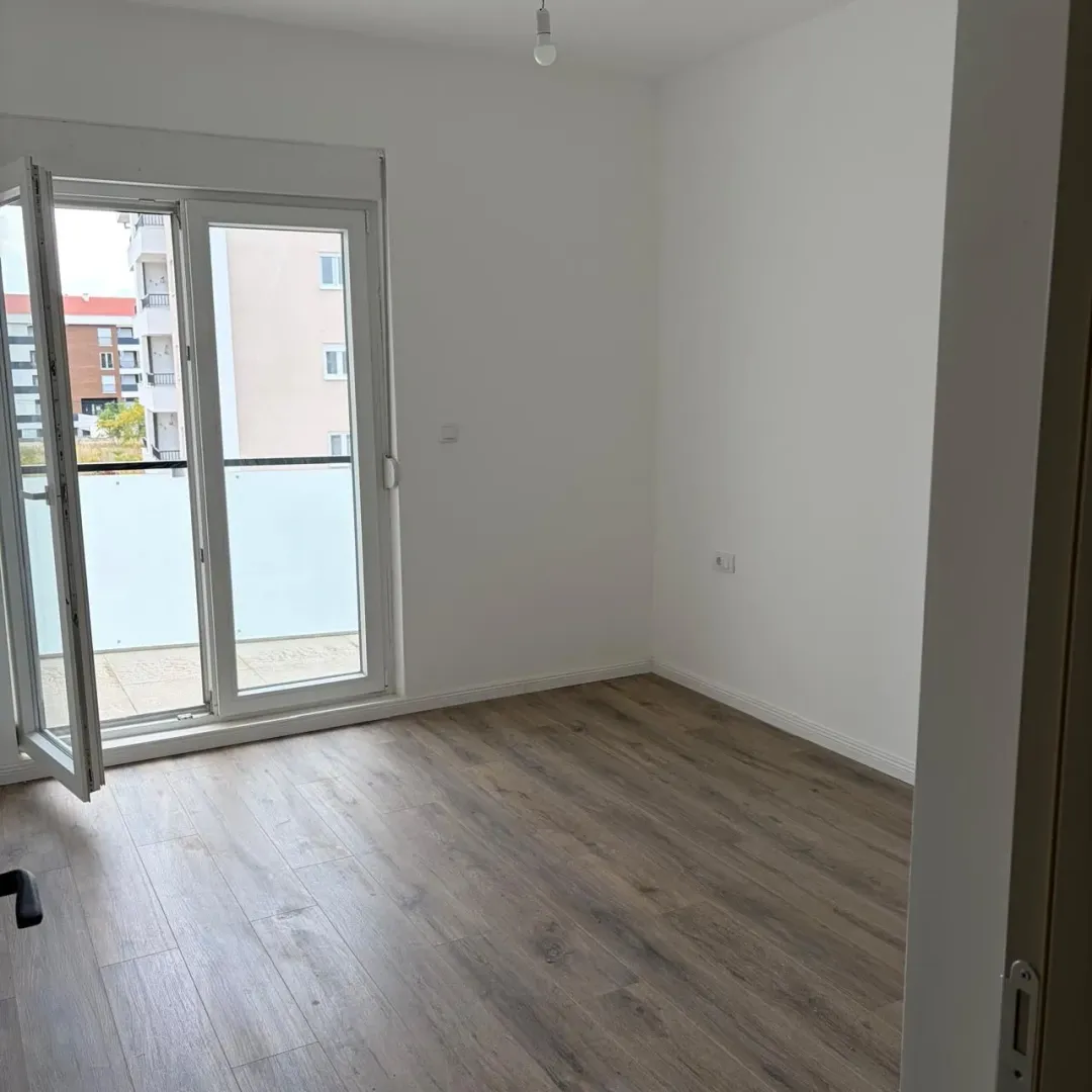 Empty room with wooden flooring and balcony doors.