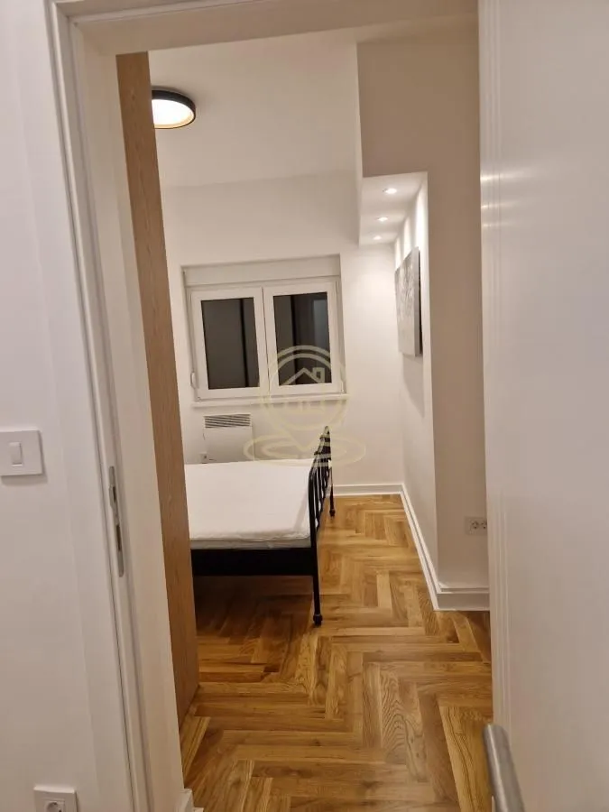 Pogled iz hodnika na spavaću sobu sa krevetom i parketom na podu.