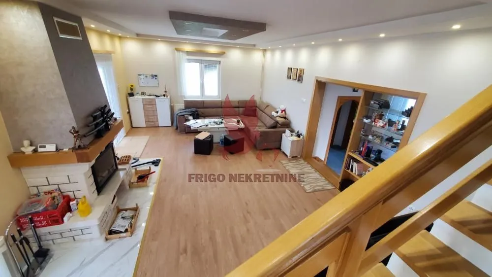 Prostrani dnevni boravak sa garniturom, kaminom i stepeništem.