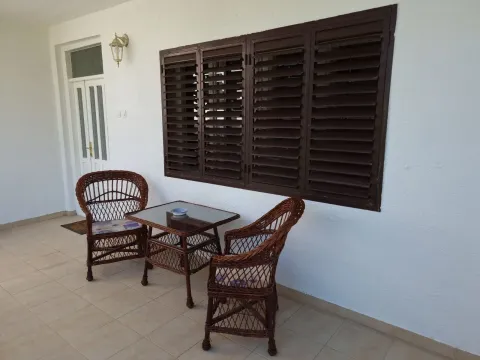 Covered terrace with wicker seating furniture in front of a white facade. - image 11