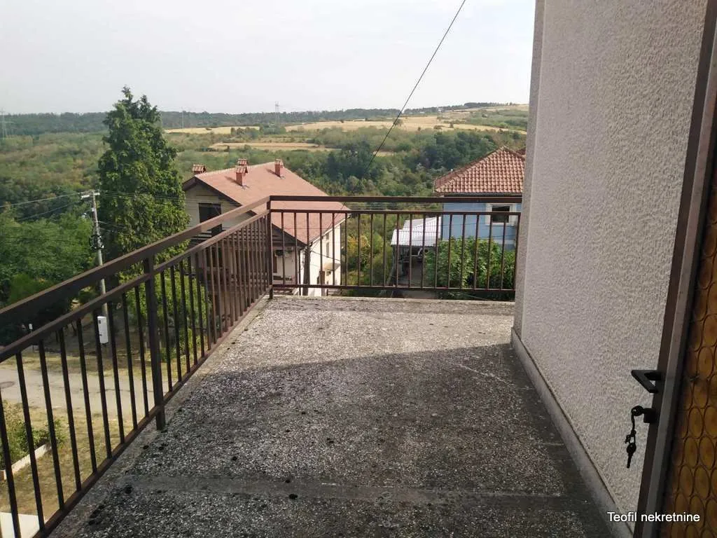 Otvorena terasa sa metalnom ogradom i pogledom na okolno zelenilo i kuće.