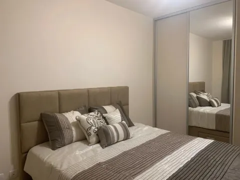 Uređena spavaća soba sa bračnim krevetom i velikim ugrađenim garderobe sa ogledalom. - image 4