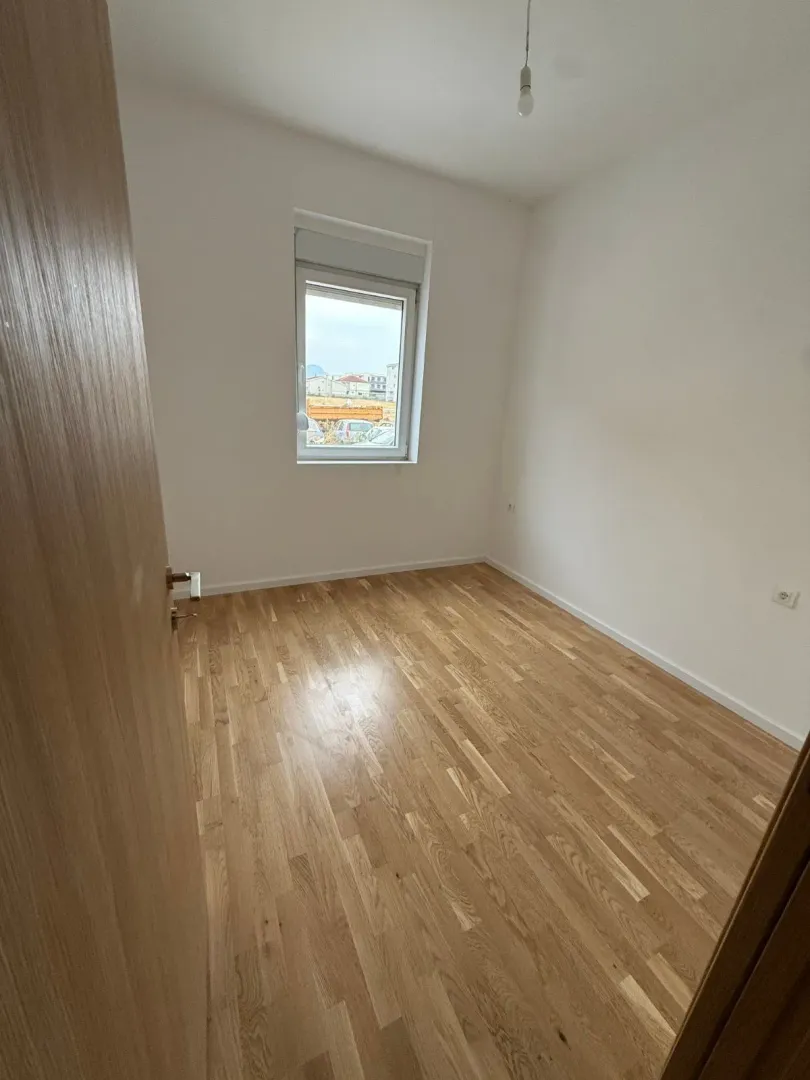 Prazna soba sa parketom i bijelim zidovima.