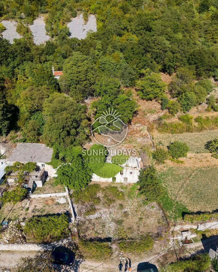 Pogled iz vazduha na staru kamenu kuću i plac okružen zelenilom.