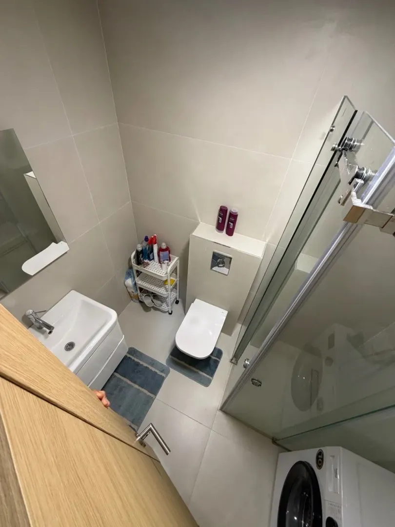 Compact bathroom with a shower cabin, washbasin, toilet, and washing machine.