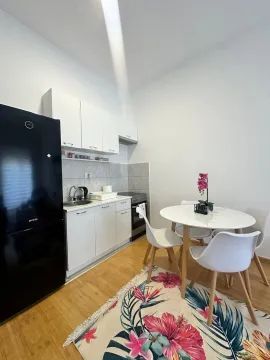 Manja bijela kuhinja sa crnim frižiderom i trpezarijskim stolom. - image 2