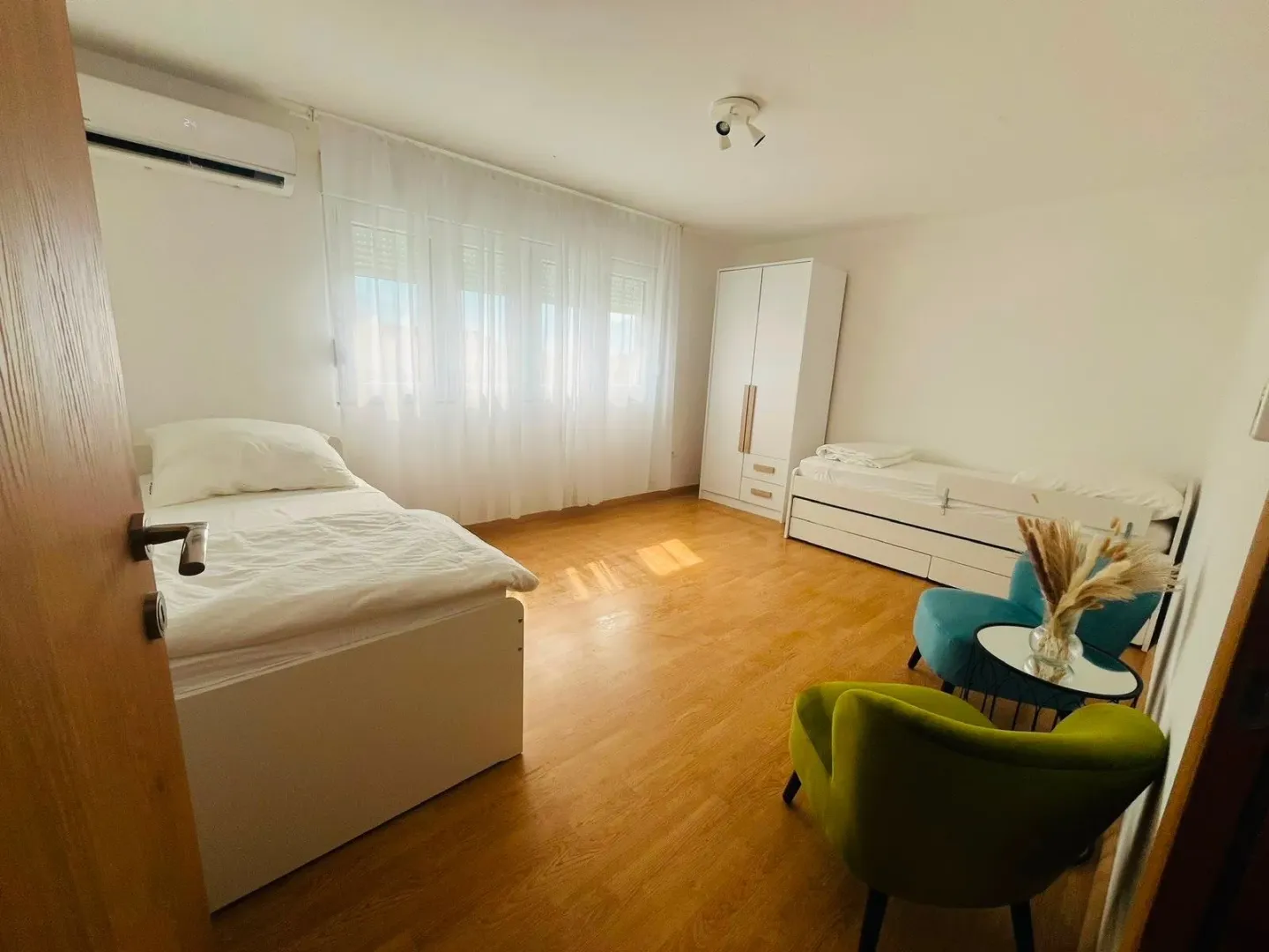 Svjetla i uredna spavaća soba sa dva kreveta, ormarom i foteljama.