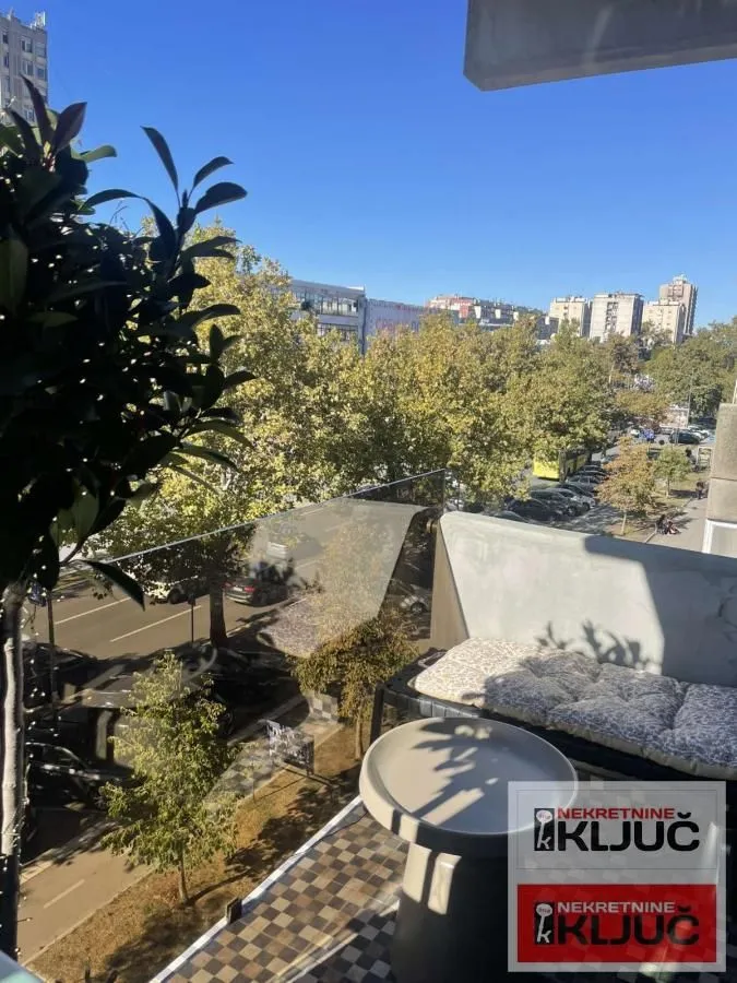 Namešten balkon sa stolom i pogledom na ulicu i drveće.
