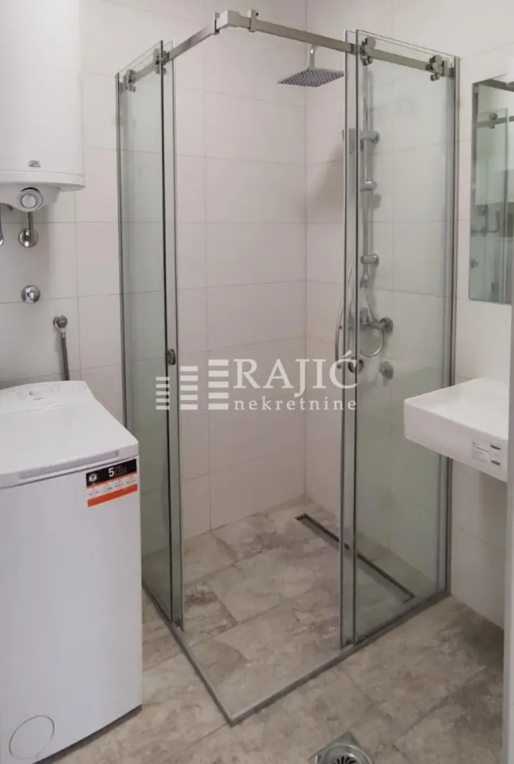 Modern bathroom with a walk-in shower, washbasin, and washing machine.