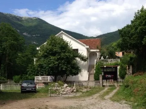 Bijela dvospratna kuća sa dvorištem okružena zelenilom i brdima u pozadini. - image 2
