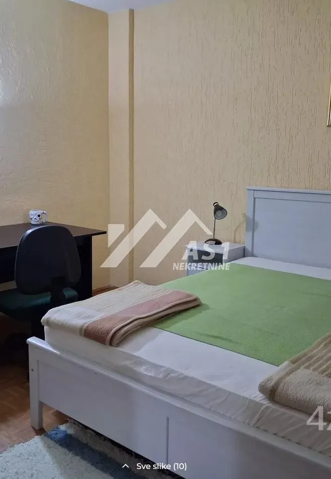 Spavaća soba sa bračnim krevetom, radnim stolom i noćnom lampom.
