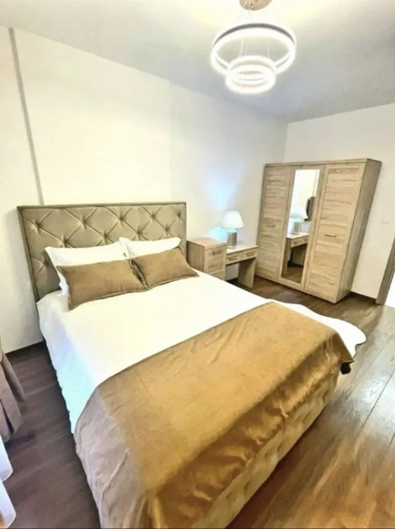 Spavaća soba sa bračnim krevetom, ormarom i modernim lusterom.