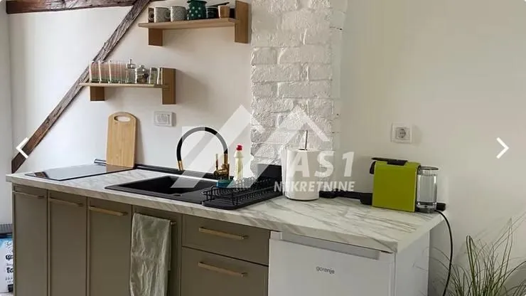 Manja kuhinja sa radnom pločom, sudoperom i drvenim policama na zidu.