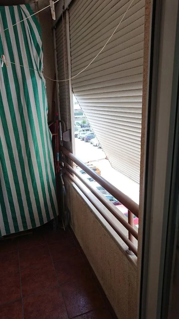 Smaller balcony with floor tiles, protective railing, and rolling shutters.