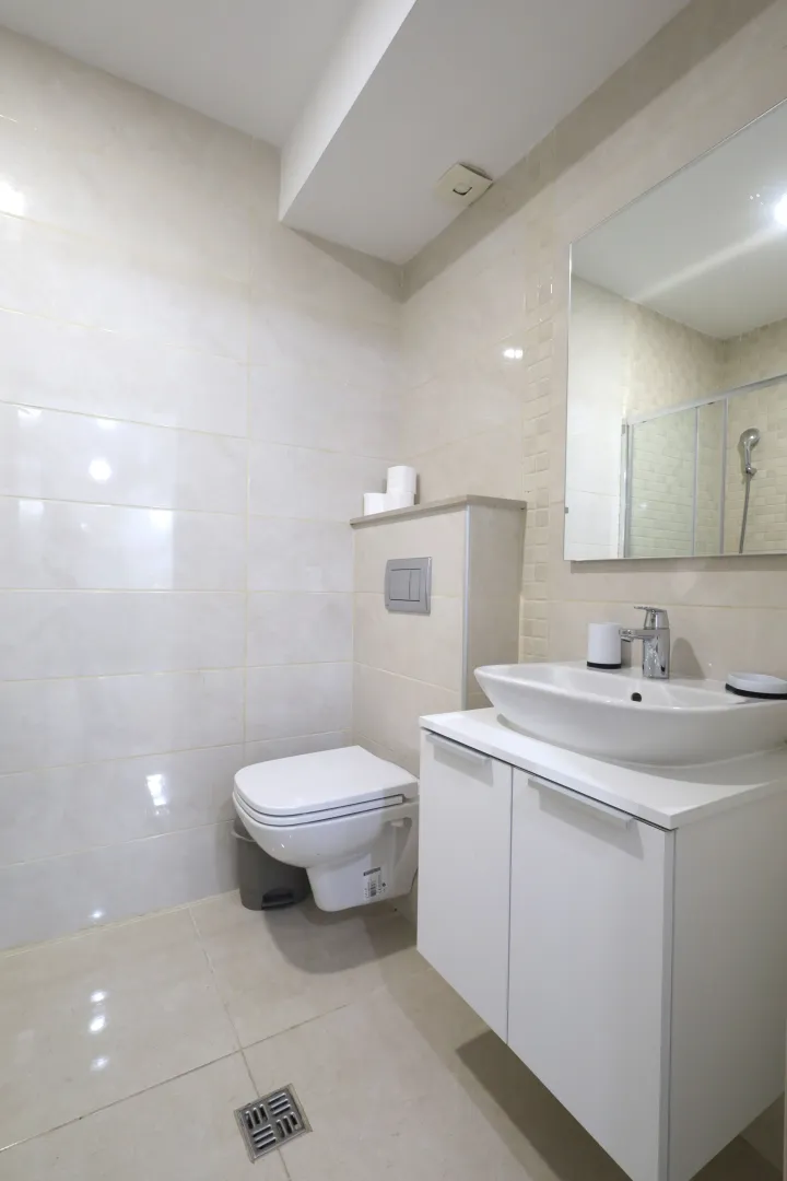 Modernly equipped bathroom with white fixtures and ceramic tiles.