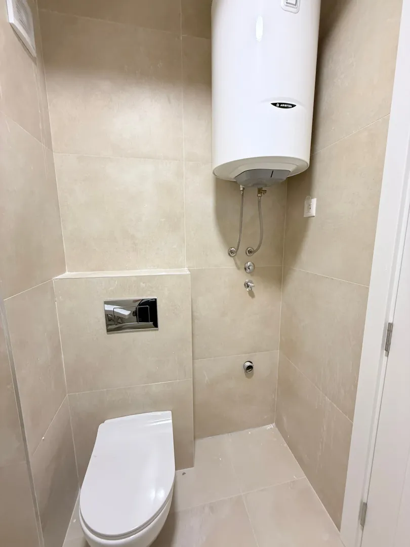 Pločicama obloženo kupatilo sa ugradnom šoljom i bojlerom.