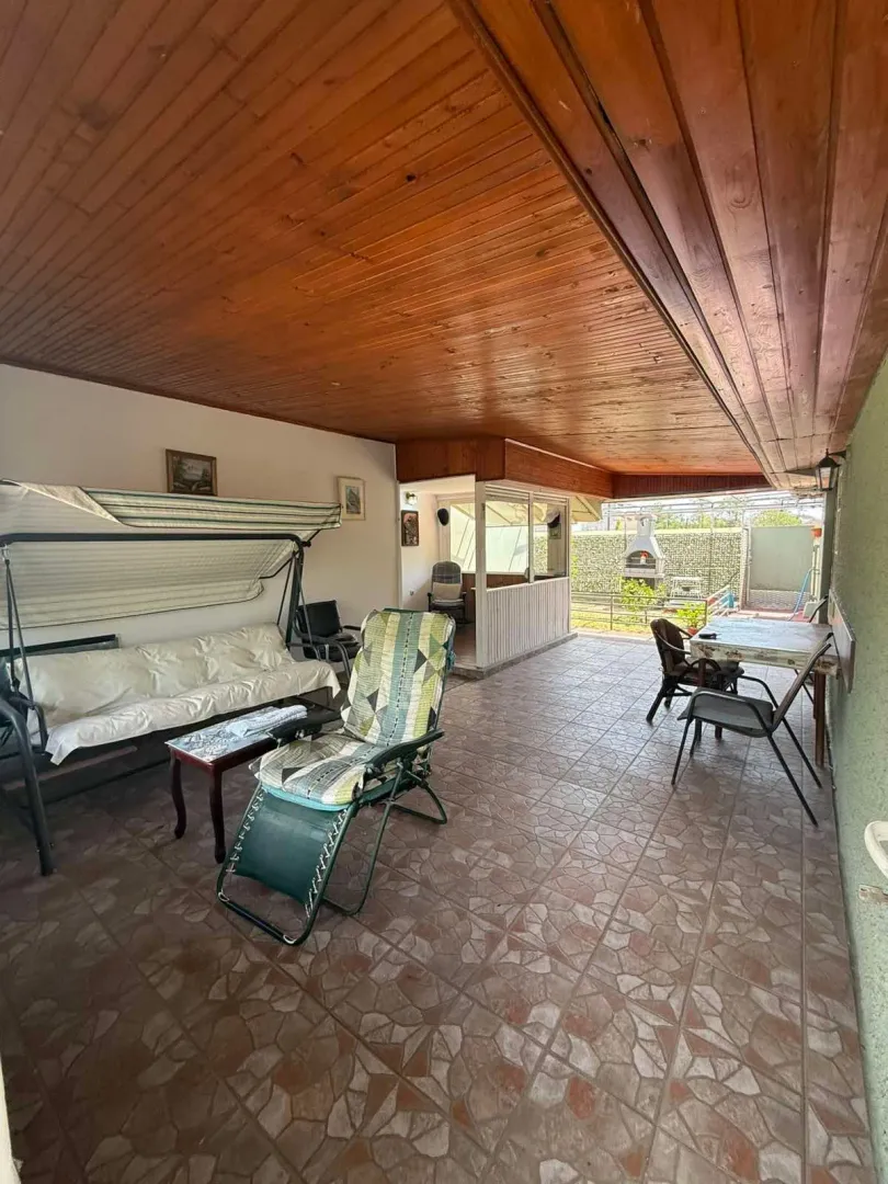 Natkrivena terasa sa garniturom za sjedenje i drvenim plafonom.