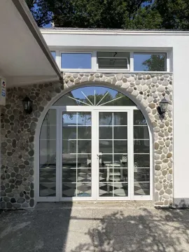 Ulaz u objekat sa lučnim staklenim vratima i kamenom dekoracijom na fasadi. - image 7