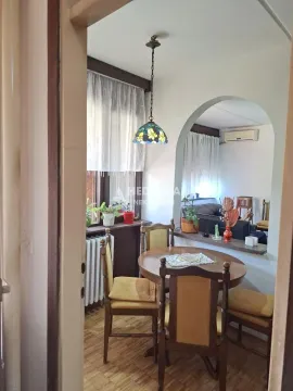 Trpezarija sa drvenim stolom i stolicama, povezana sa dnevnim boravkom kroz luk. - image 3